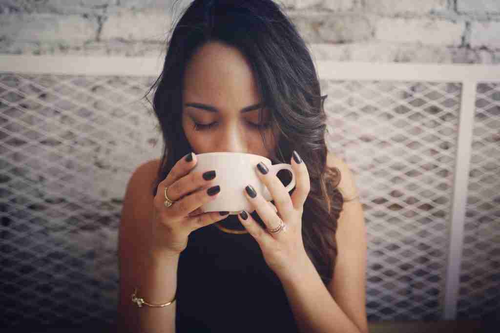 a brunette woman sipping coffee out of a white mug