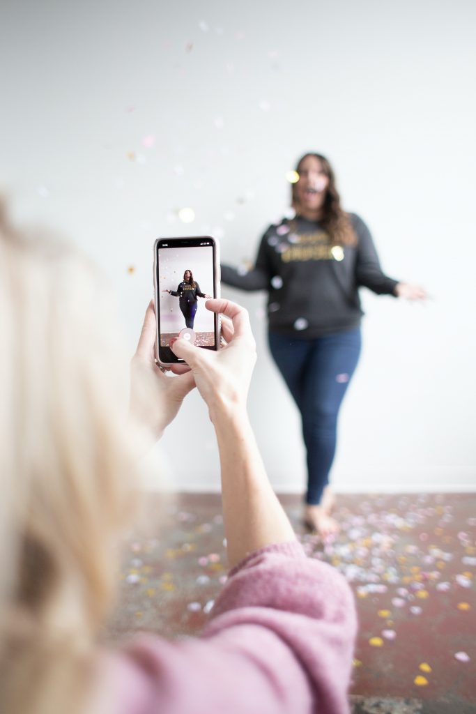 a girl taking a picture of another girl with confetti raining down on her