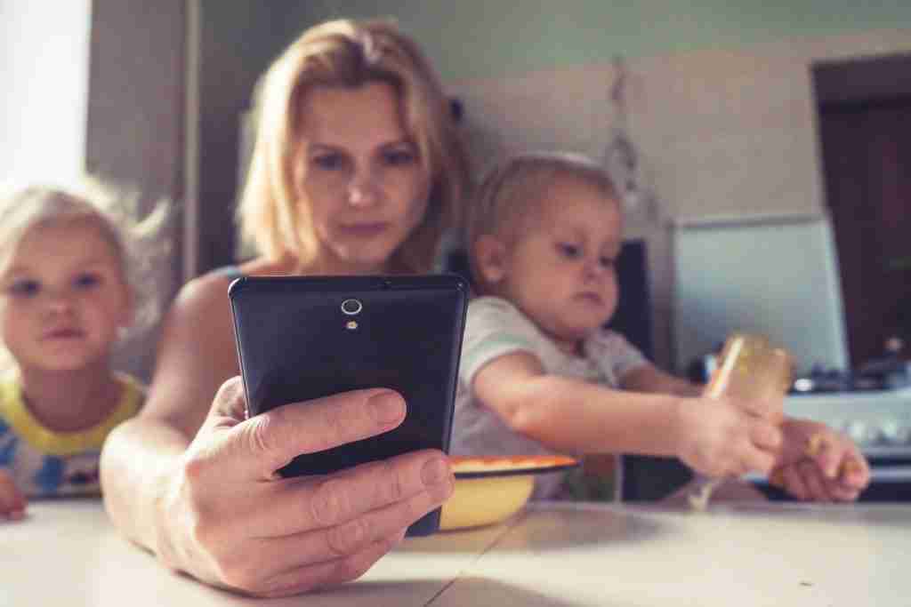 a woman with 2 babies trying to text on her phone