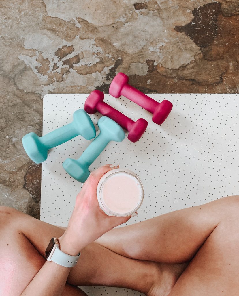 above shot of a girl holding a pink shake surrounded by weights