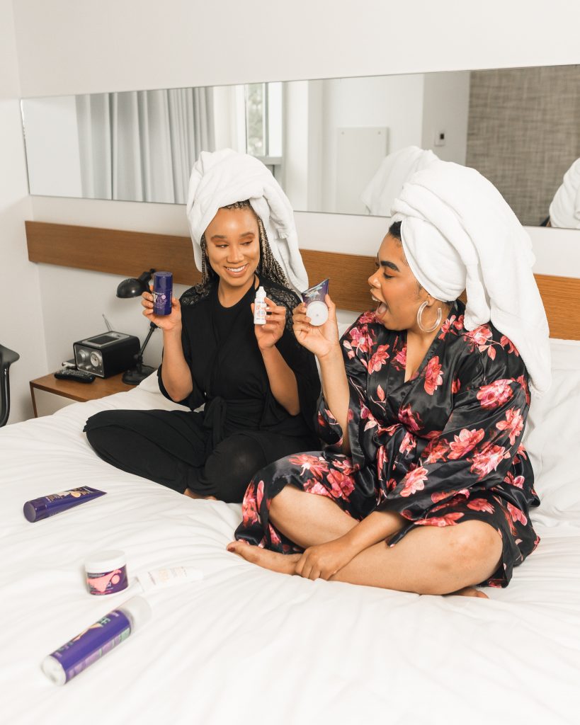 two women sat in bed and posing with makeup
