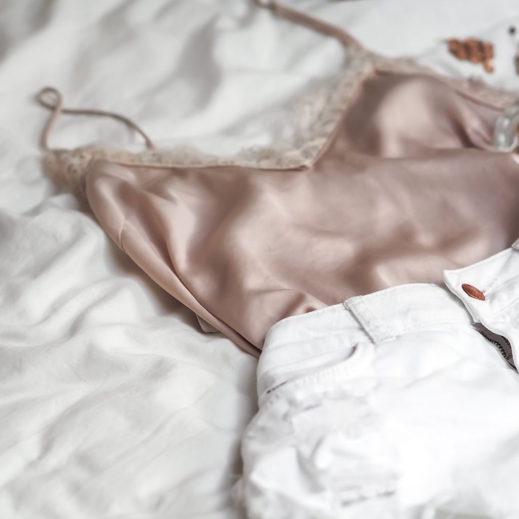 a pink silk camisole and white jeans on a bed