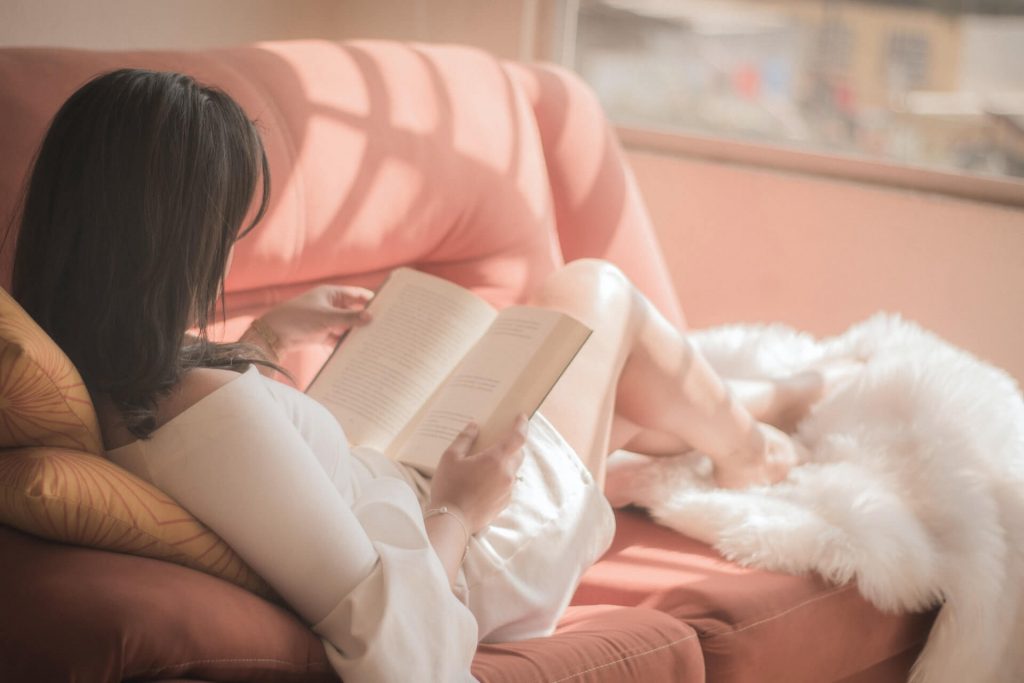 a girl reading a book on a pink couch